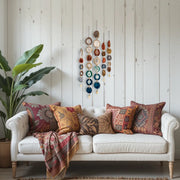 White sofa with patterned cushions and a colorful blanket in a room with wooden walls and decorative elements.