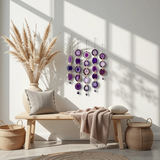 Decorative wall hanging with purple and pink elements in a sunlit room with a wooden bench, pillows, and baskets.
