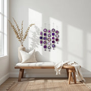 Decorative wall hanging with purple and gold elements in a bright room with a wooden bench and vase.