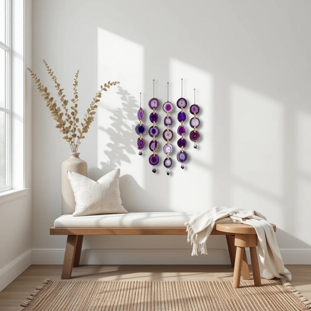 Decorative wall hanging with purple and gold elements in a bright room with a wooden bench and vase.