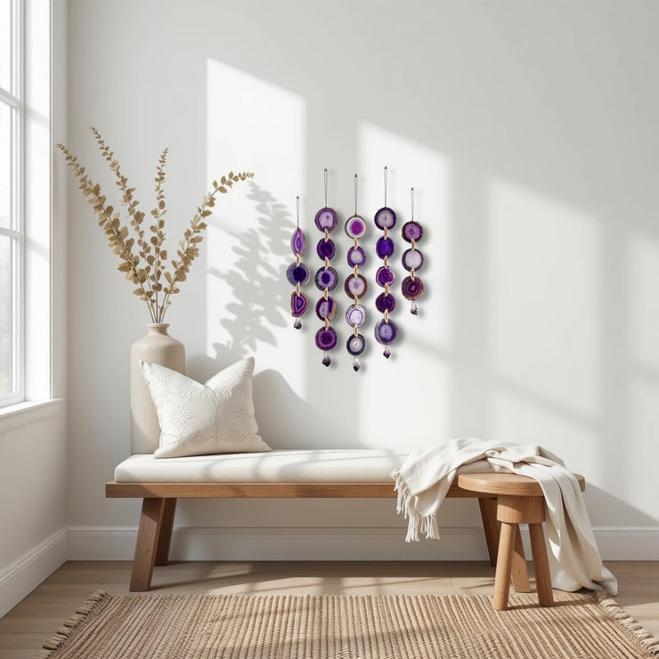 Decorative wall hanging with purple and gold elements in a bright room with a wooden bench and vase.